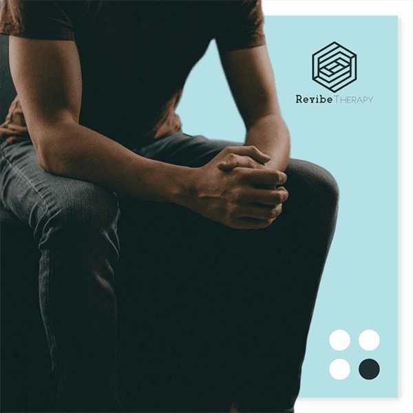 A seated person, wearing a dark red t-shirt and jeans, rests their clasped hands on their knees. The image includes a light blue background with the “Revibe Therapy” logo and four circles in varying shades of blue and white. A seated person, wearing a dark red t-shirt and jeans, rests their clasped hands on their knees. The image includes a light blue background with the "Revibe Therapy" logo and four circles in varying shades of blue and white.