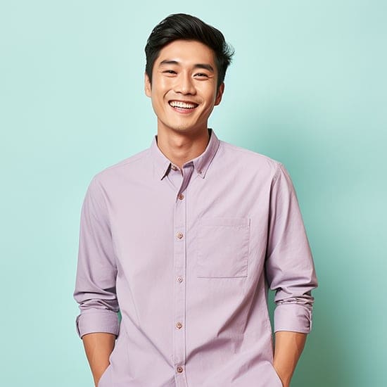 A smiling man stands in front of a light turquoise background, wearing a light purple button-up shirt with the sleeves rolled up. His hands are in his pockets, and he exudes a cheerful and relaxed vibe. A smiling man stands in front of a light turquoise background, wearing a light purple button-up shirt with the sleeves rolled up. His hands are in his pockets, and he exudes a cheerful and relaxed vibe.