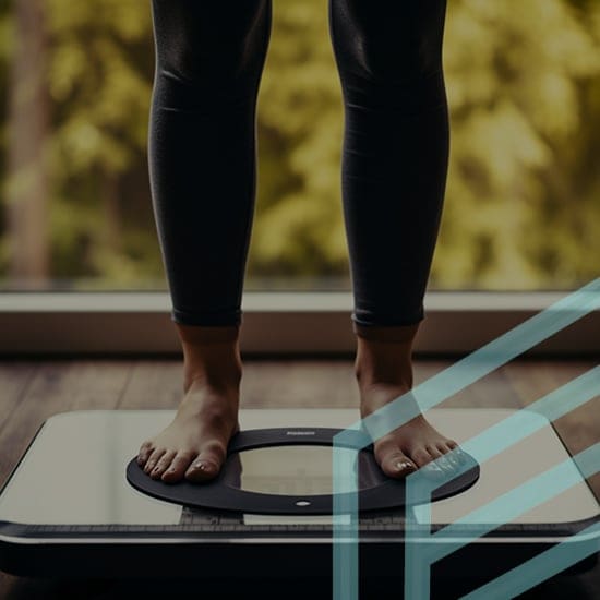 A person stands on a digital scale indoors, measuring their weight. The background is blurred with a view of green foliage outside a window. The person's lower legs and feet are visible, and there is a translucent overlay of geometric patterns.