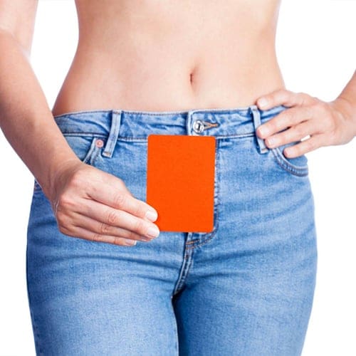 A person in blue jeans is showing an orange card, holding it in front of their abdomen with one hand while the other hand rests on their hip. The background is white, and their midriff is visible. A person in blue jeans is showing an orange card, holding it in front of their abdomen with one hand while the other hand rests on their hip. The background is white, and their midriff is visible.