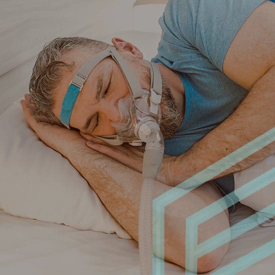 A man with short gray hair lies on his side in bed, wearing a blue t-shirt and a CPAP mask with a head strap that holds it in place. His head rests on a white pillow as he appears to be sleeping. The image is overlaid with partial geometric designs.