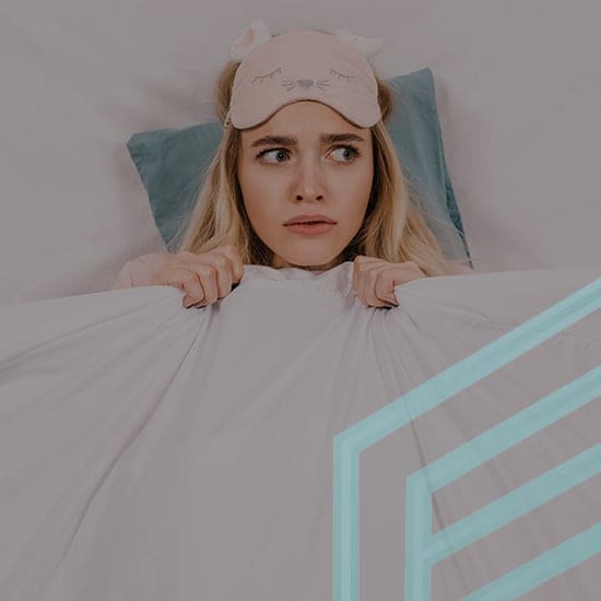 A woman with long blonde hair wearing a pink sleep mask lies in bed, holding a white blanket up to her chin with a worried expression on her face. The background is light grey, and there's a light blue geometric design overlaid on the bottom right corner.