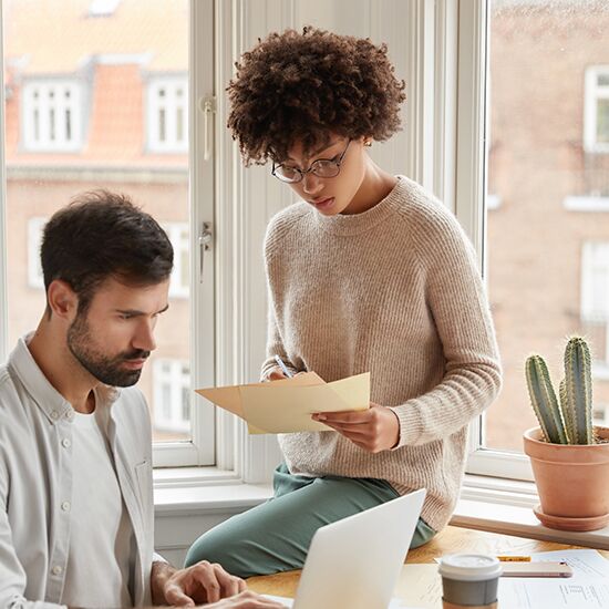 Multiethnic designers pose against window, discuss ideas for project, sit in coworking space, search information on laptop compuer, fill in documentation. Mixed race student prepare for exam testing